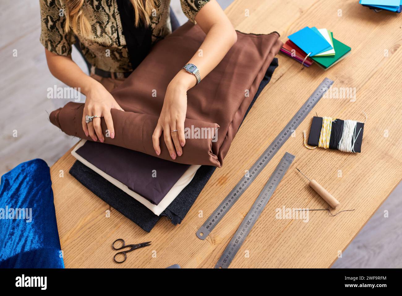 cropped view of clothes stylist checking fabrics samples near sewing supplies in fashion atelier Stock Photo