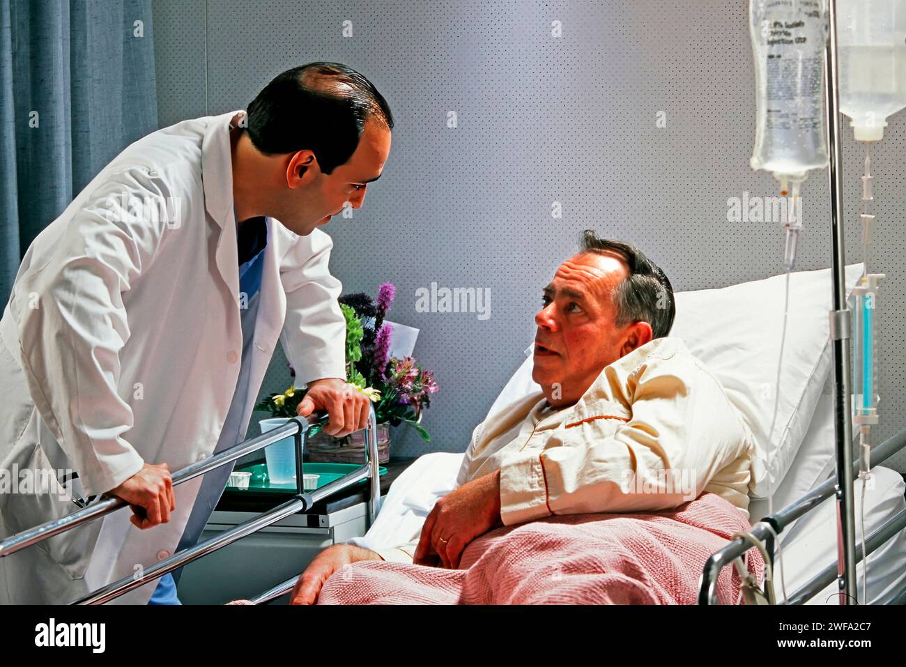 A man in a hospital bed engaged in conversation with a medical professional wearing a white coat. Stock Photo