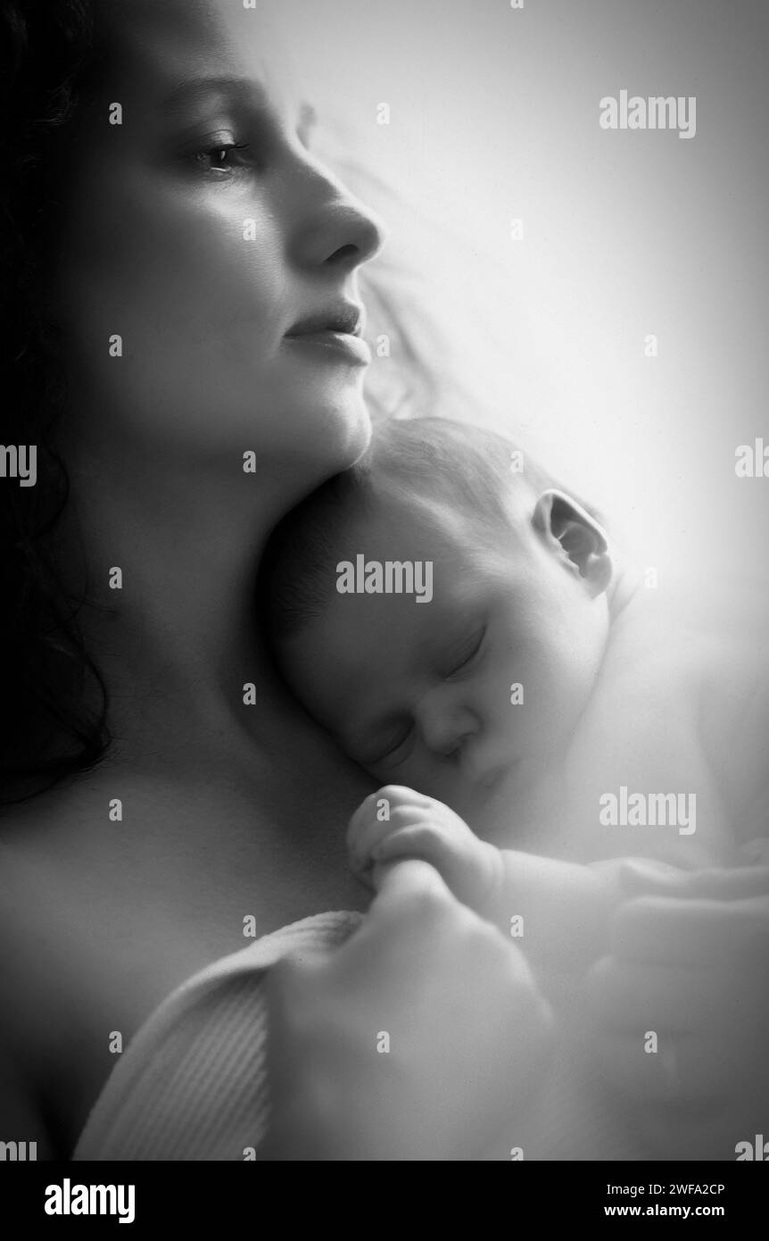 A black-and-white photograph of a woman gently cradling a newborn baby in her arms, creating a tender moment of love and care. Stock Photo