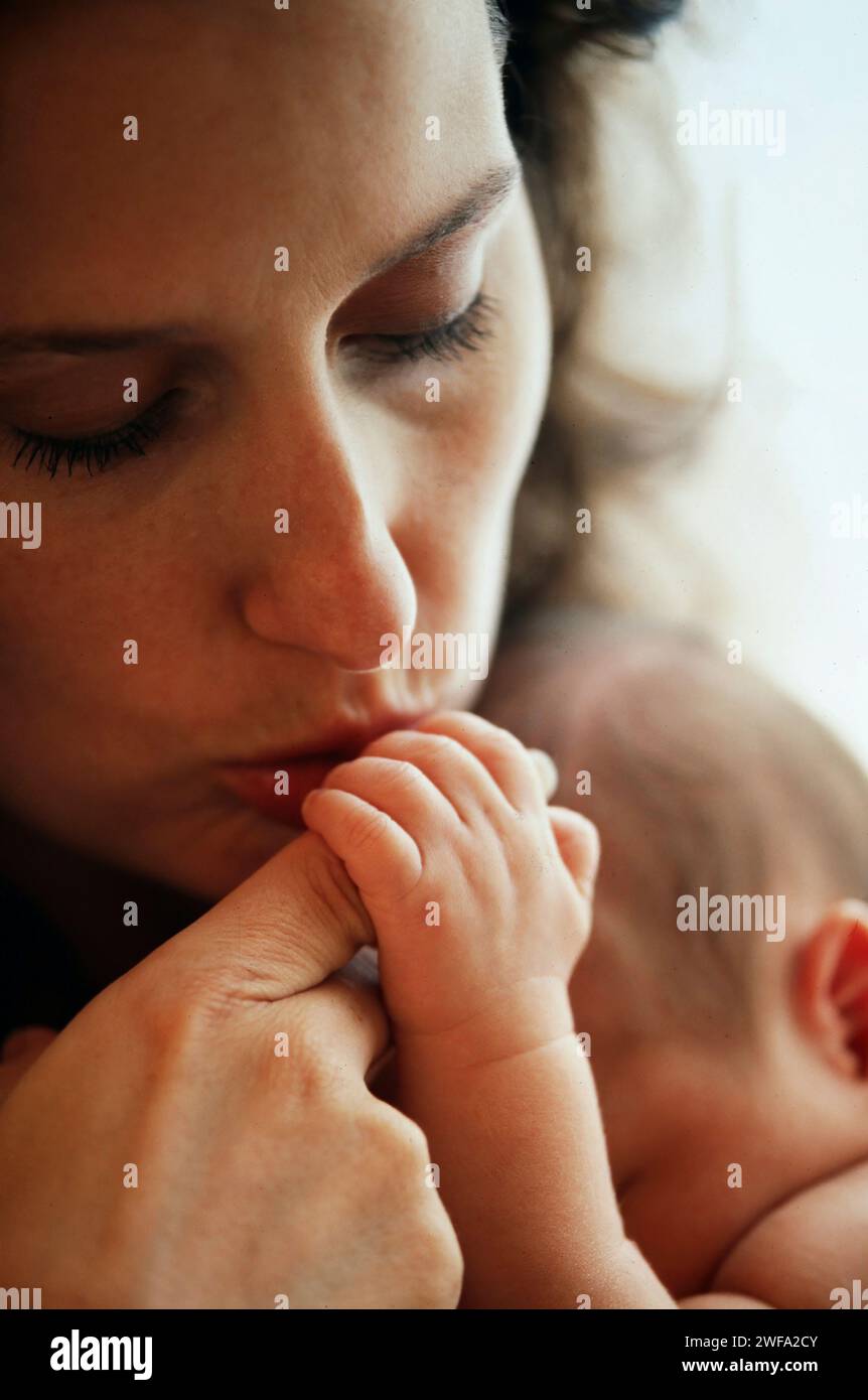 Unattractive mother gently kissing the hand of her newborn baby Stock Photo