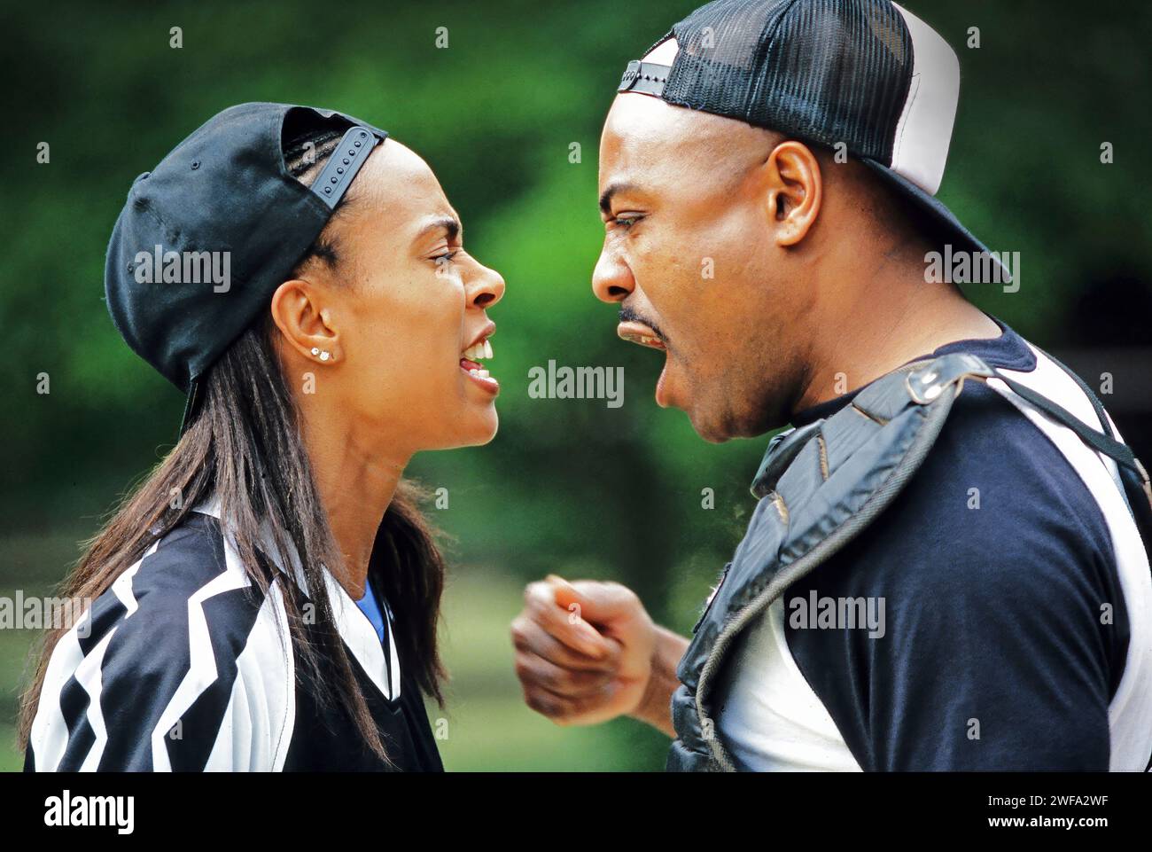 Two african-American baseball players engaged in a heated argument showing expressive gestures and emotions, against an outdoor, blurred  background. Stock Photo