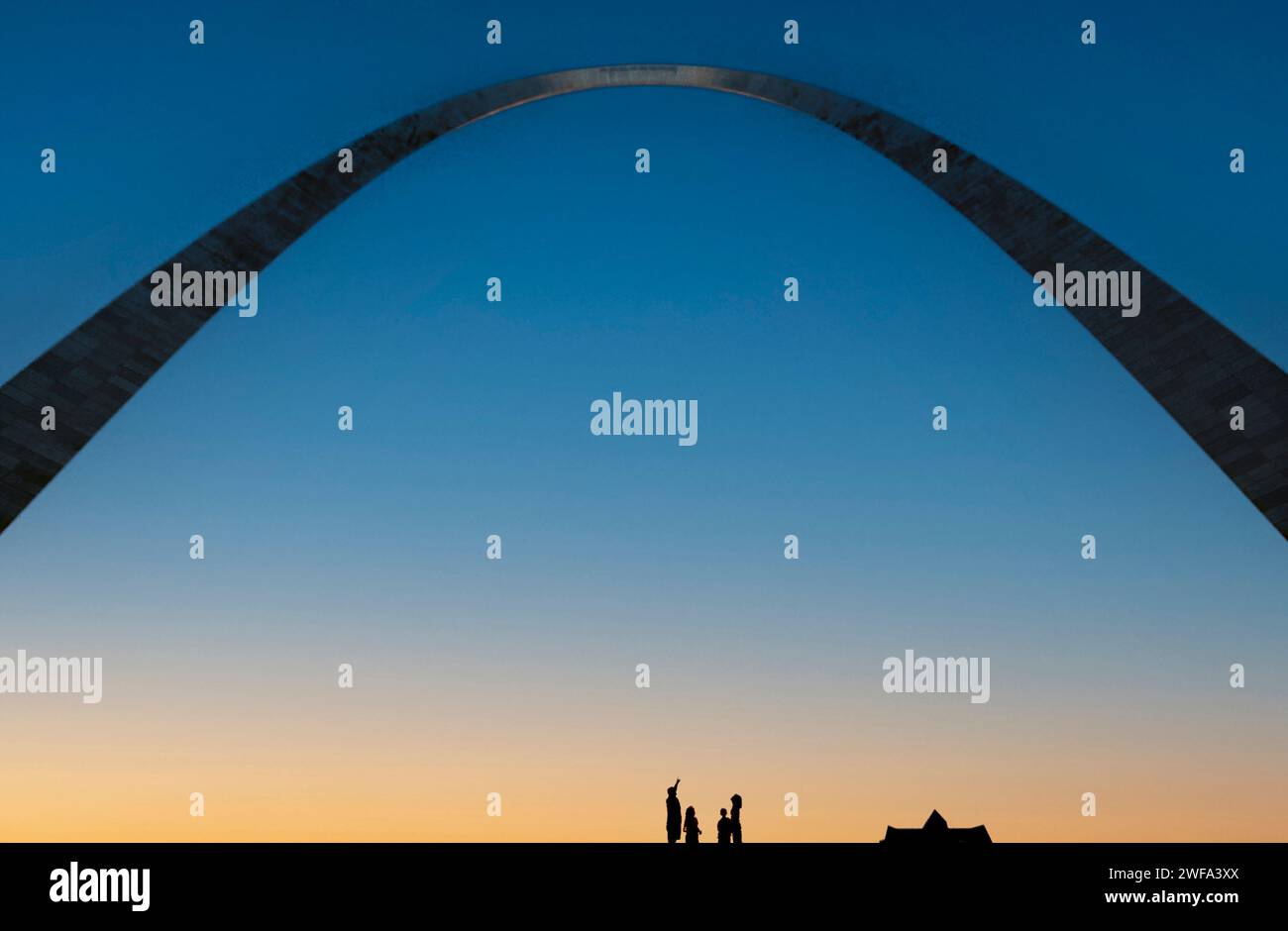 A group of people are silhouetted against the twilight sky underneath the iconic Gateway Arch in St. Louis, Missouri. Stock Photo