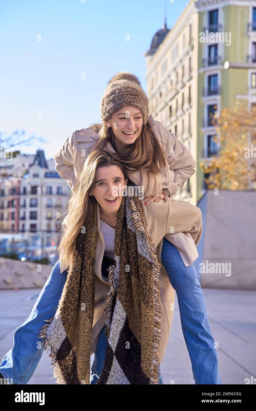Laughing young female friends piggy back riding outdoors on a residential urban street Stock Photo