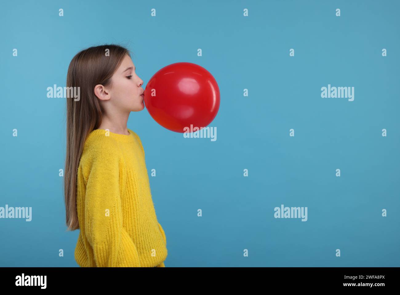 Cute girl inflating red balloon on light blue background, space for ...