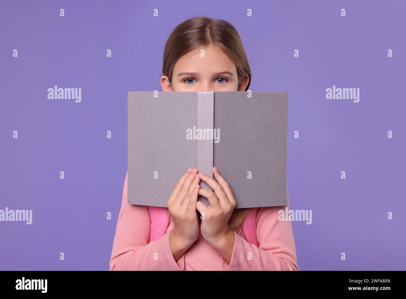 Cute schoolgirl with open book on violet background Stock Photo - Alamy
