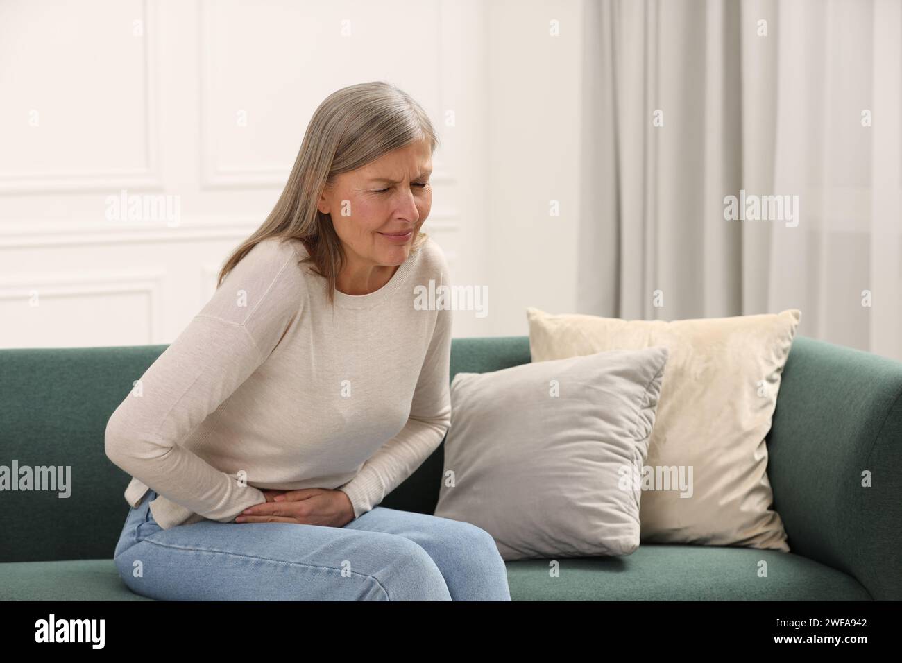 Menopause. Woman suffering from abdominal pain on sofa at home Stock