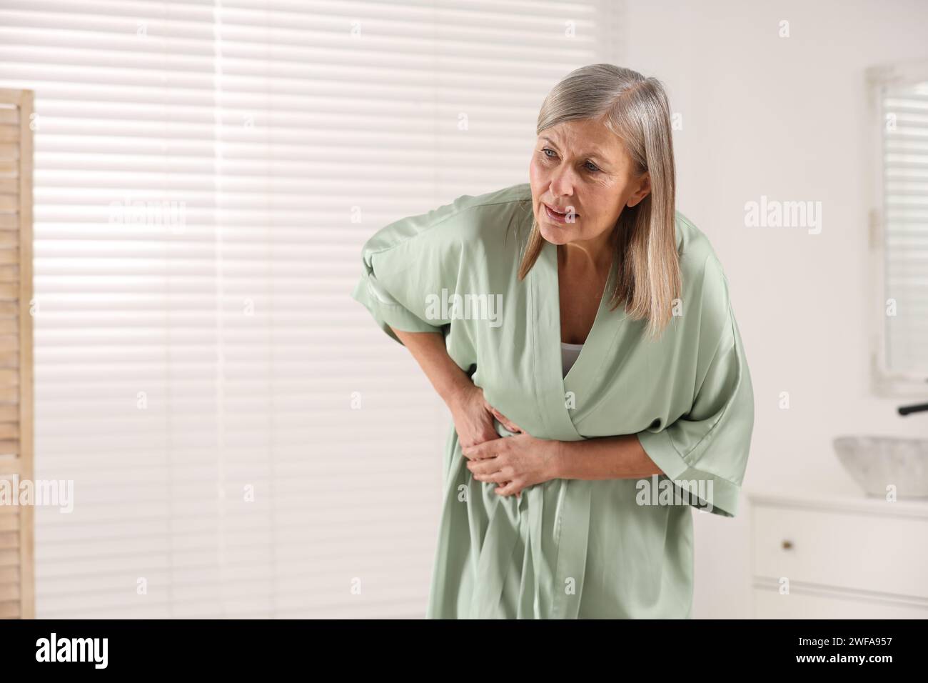 Menopause. Woman suffering from digestive problems in bathroom, space