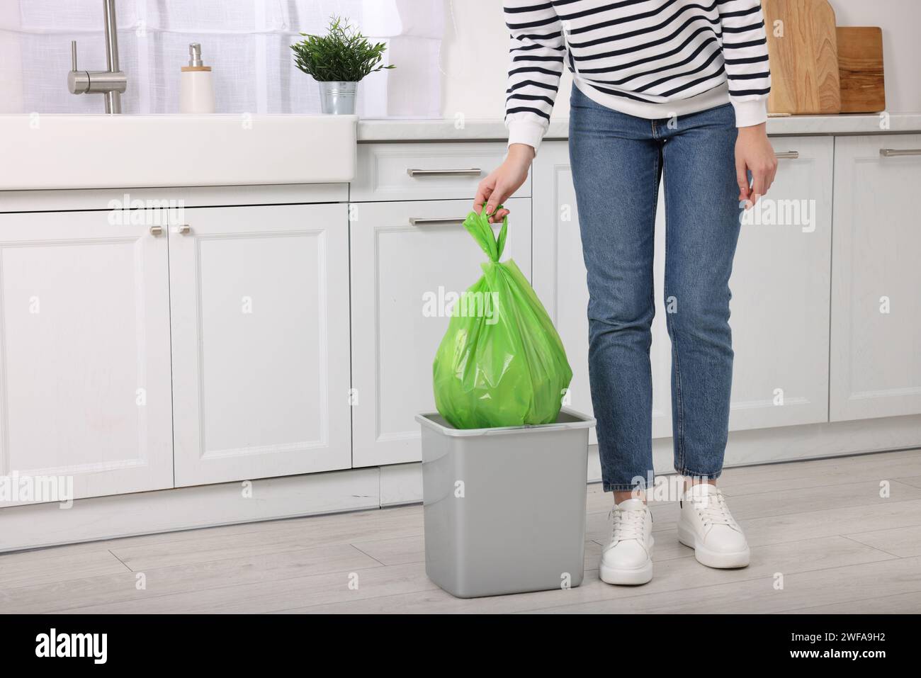 Woman taking garbage bag out of trash bin in kitchen, closeup. Space for text Stock Photo
