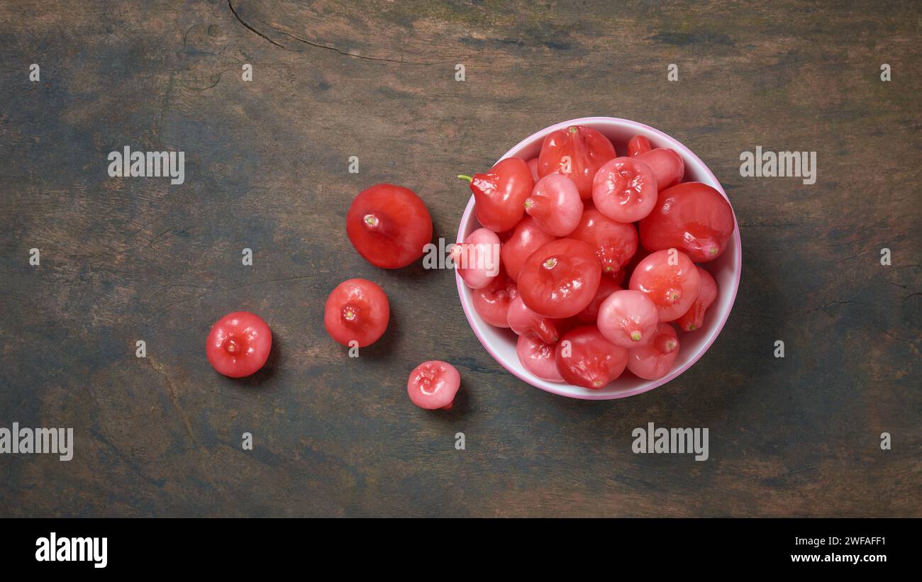 jambu or rose apple, aka bell fruit or wax apple, flesh is crisp and watery, cup full of bell-like or pear shaped juicy fruits on wooden table surface Stock Photo