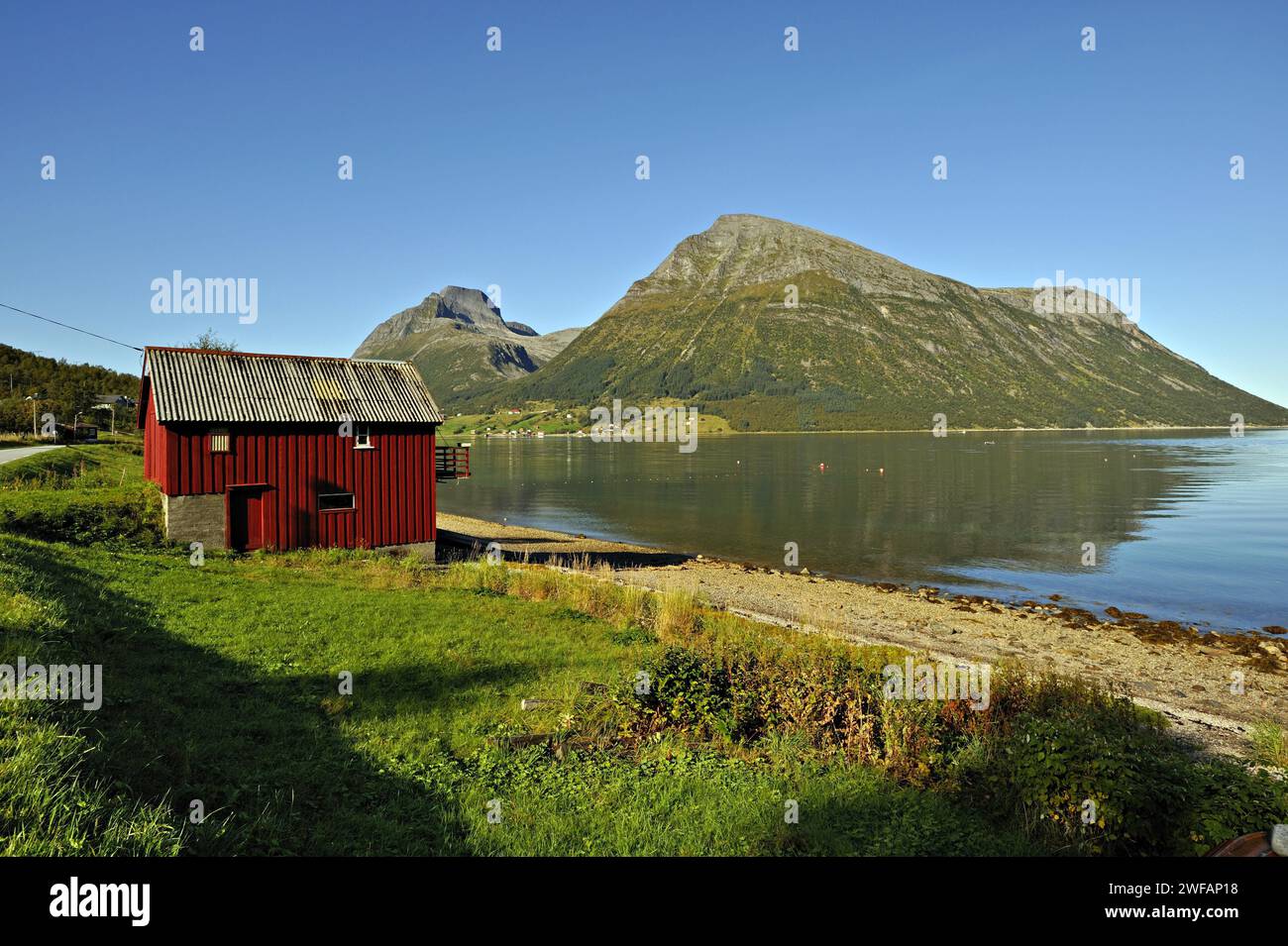 Red wooden boathouse at Lia with the island of Aldra and the Hjarttinden peaks behind, north-west Norway Stock Photo