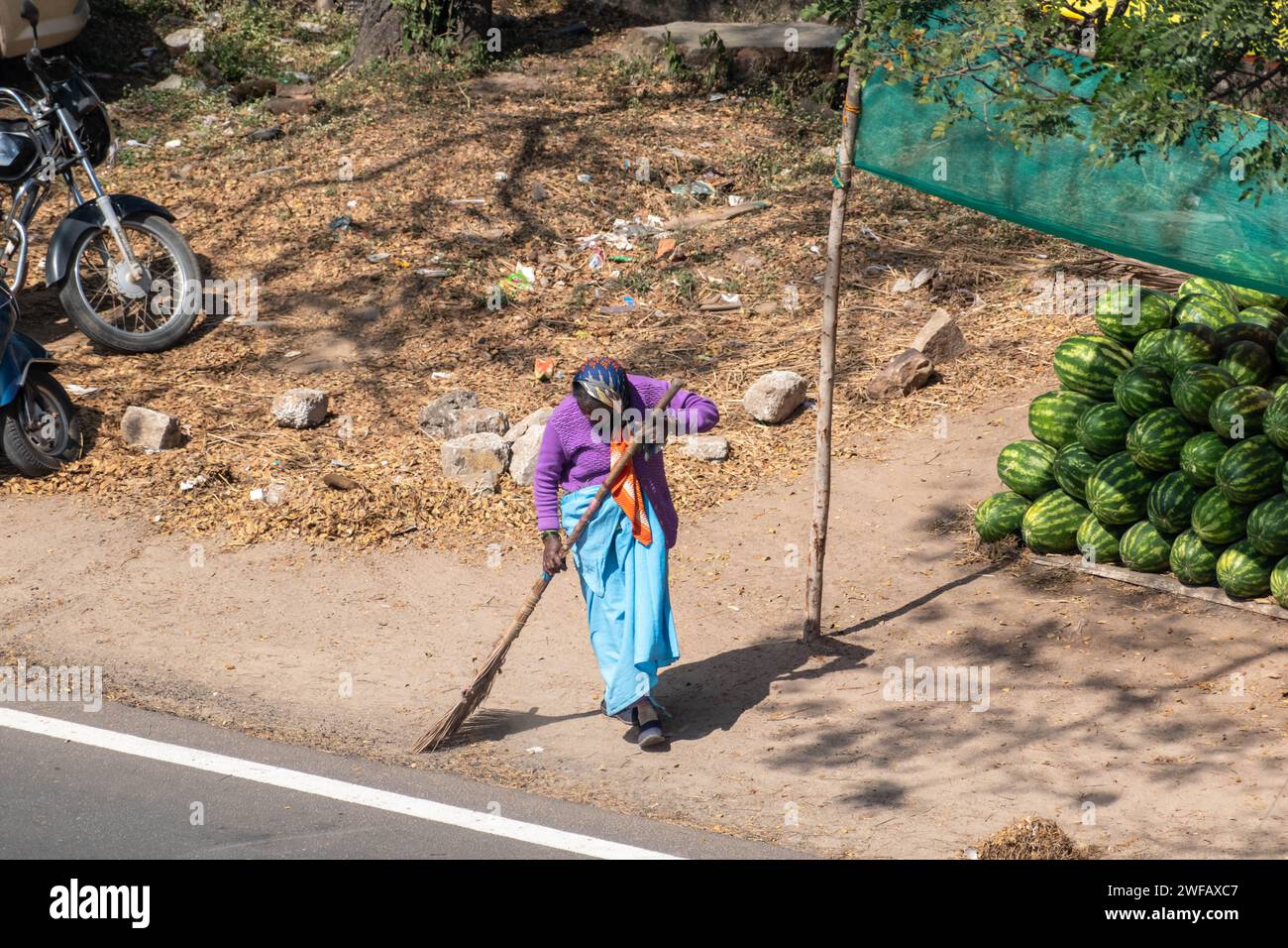 Hassan, Karnataka, India - January 9 2023: An Indian woman sanitation worker sweeping a street with a broom. Stock Photo