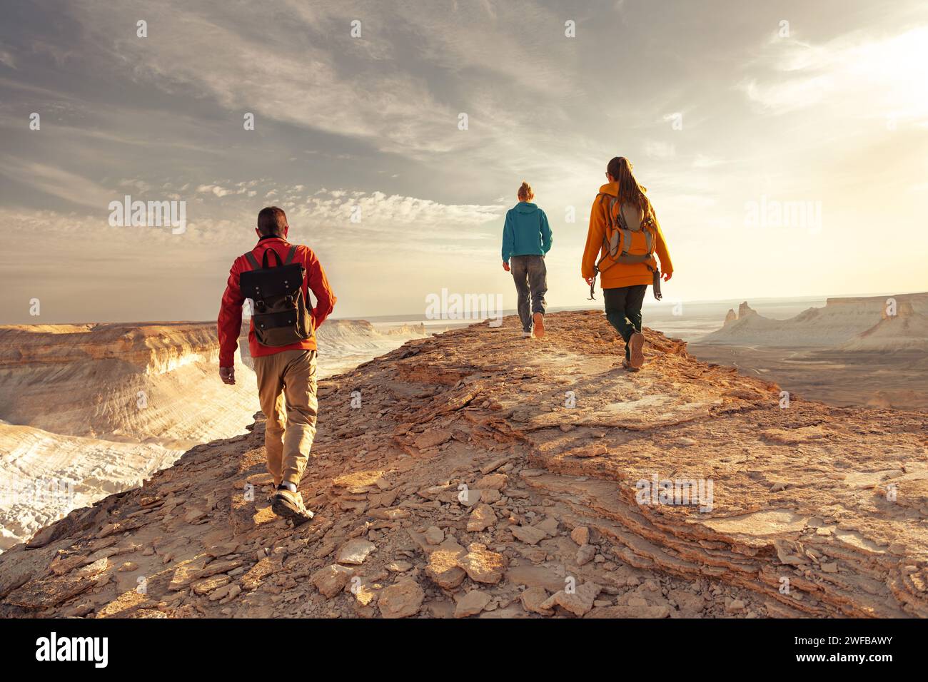 Three young tourists with backpacks are walking at sunset mountain top with awesome view Stock Photo