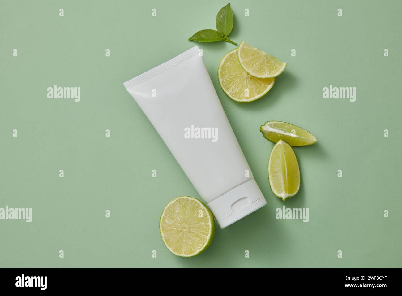 An empty label white tube decorated with Lime several Lime slices over a pastel background. Lime (Citrus aurantiifolia) is high in vitamin C, antioxid Stock Photo