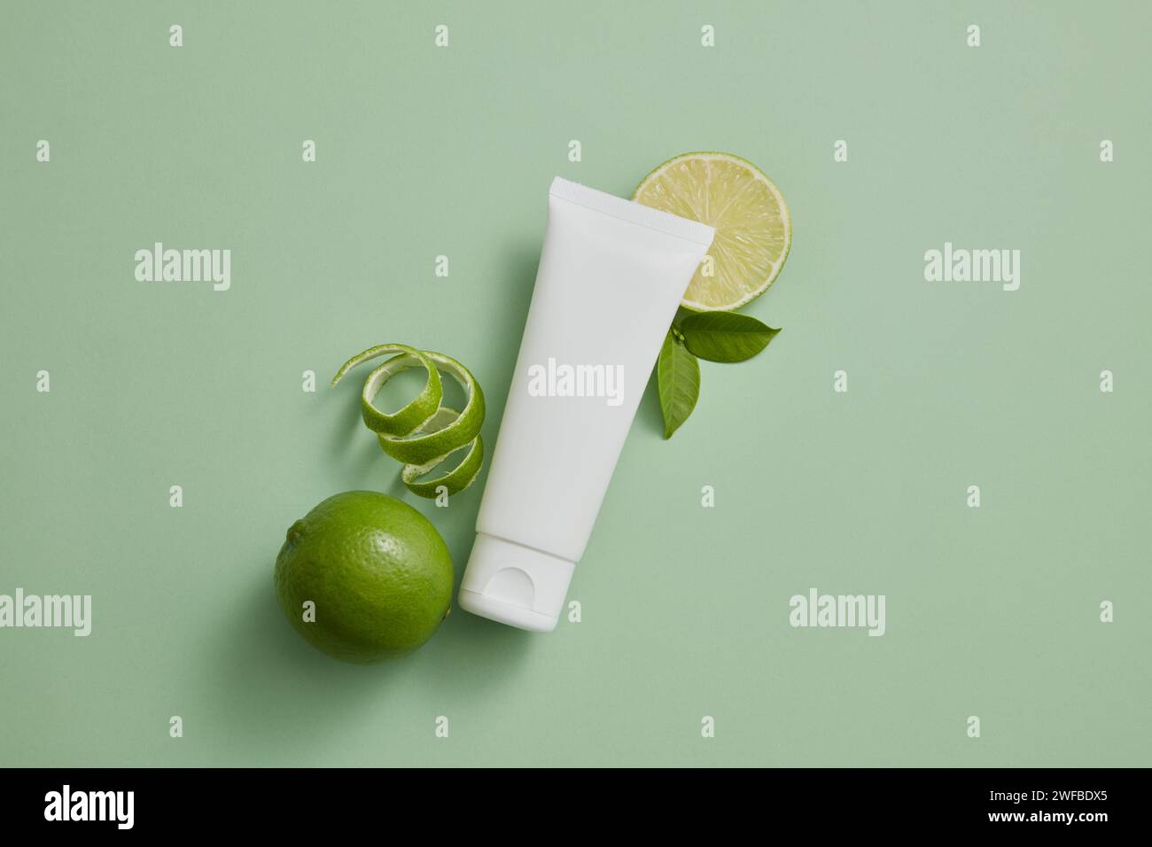 An unlabeled tube in white color displayed with Lime slices and peel. Lime (Citrus aurantiifolia) essential oil can remove dead cells that accumulate Stock Photo