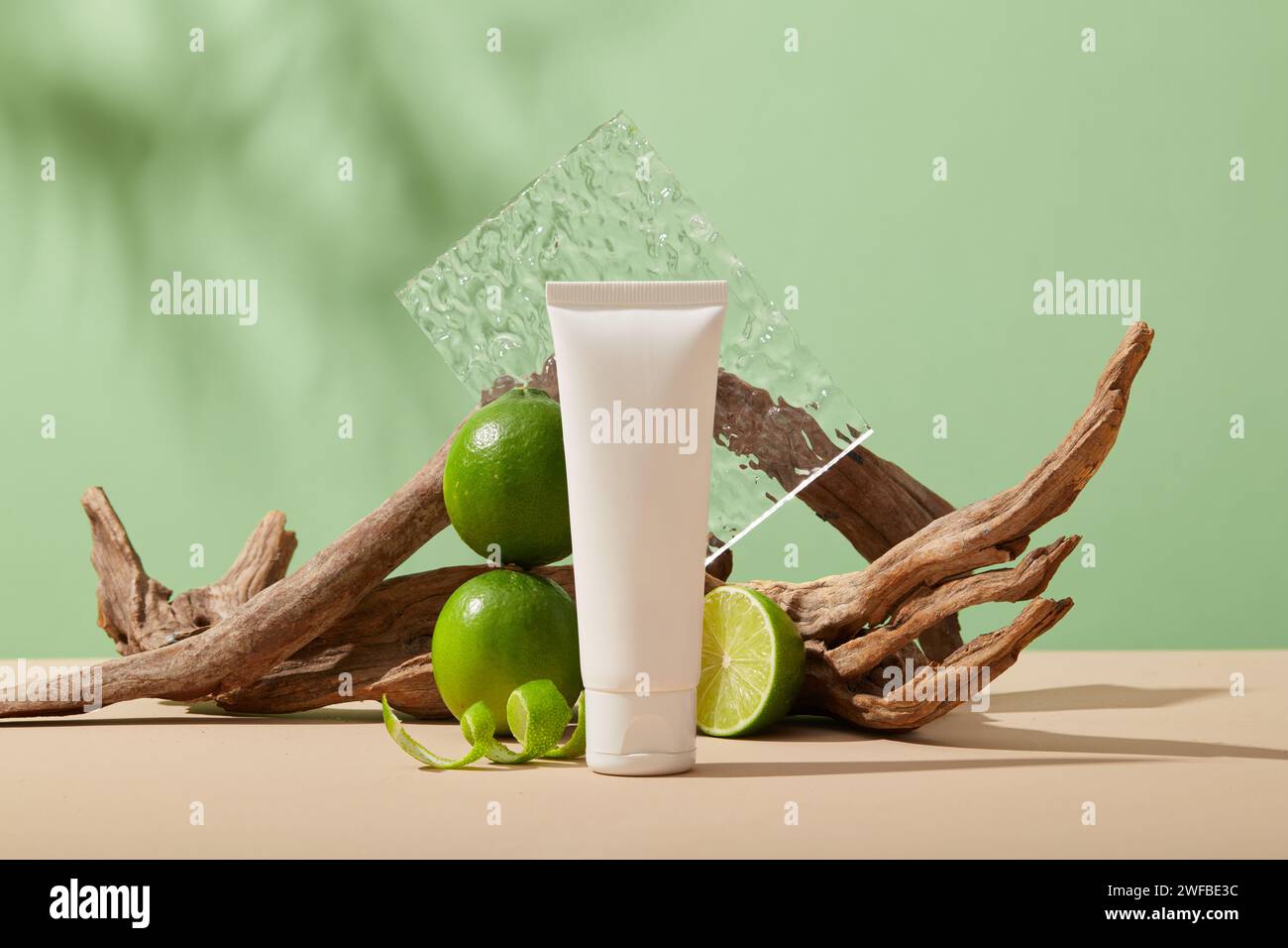 A white tube without label arranged with Lime slice and peels against pastel green background. Lime (Citrus aurantiifolia) is high in vitamin C that c Stock Photo