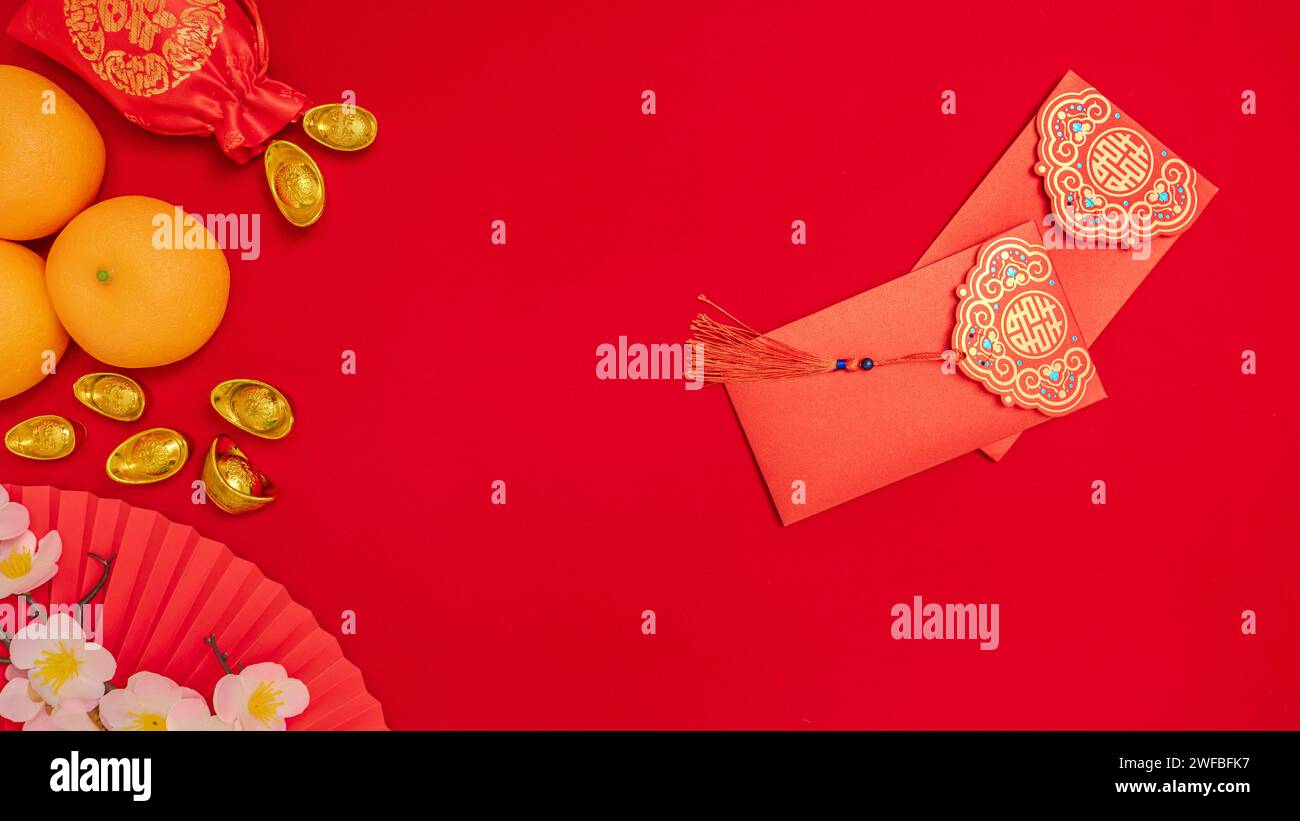 Chinese Lunar New Year background, red theme. silk bag with ancient gold bar, orange, paper hand fan, plum blossom branch, red envelope Stock Photo