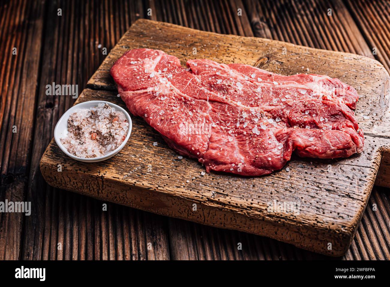 Raw Chuck eye beef steak seasoned with salt and pepper on wooden cutting board Stock Photo