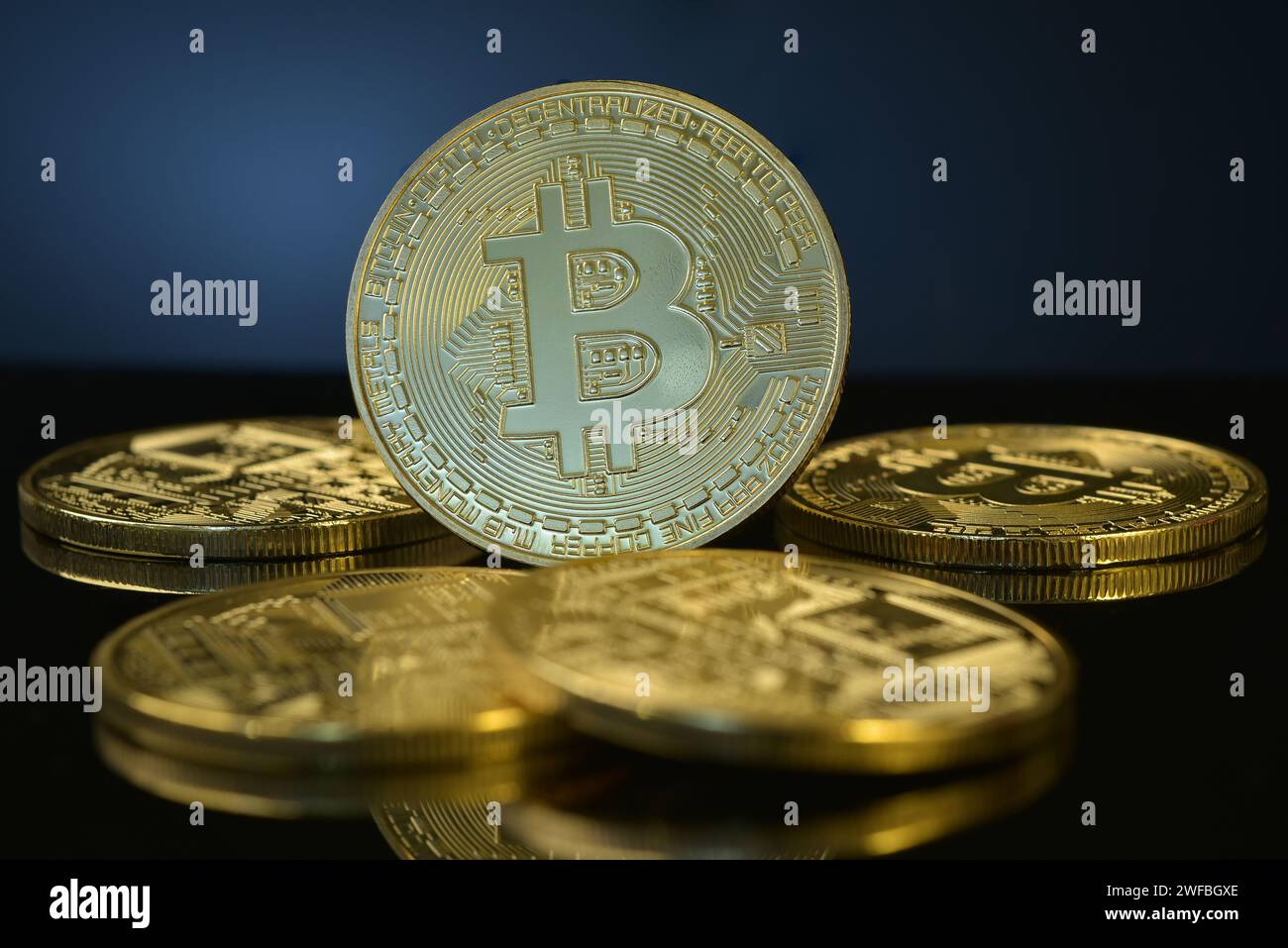 Photograph of golden Bitcoin isolated on black reflective background, surrounded by pile of coins. Cryptocurrency. Decentralised digital currency. Stock Photo