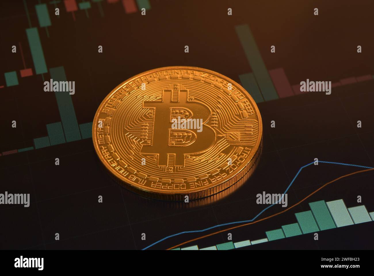 Single golden Bitcoin close up lying flat and price chart with green vol and macd lines on background. Technical analysis in cryptocurrency. Stock Photo