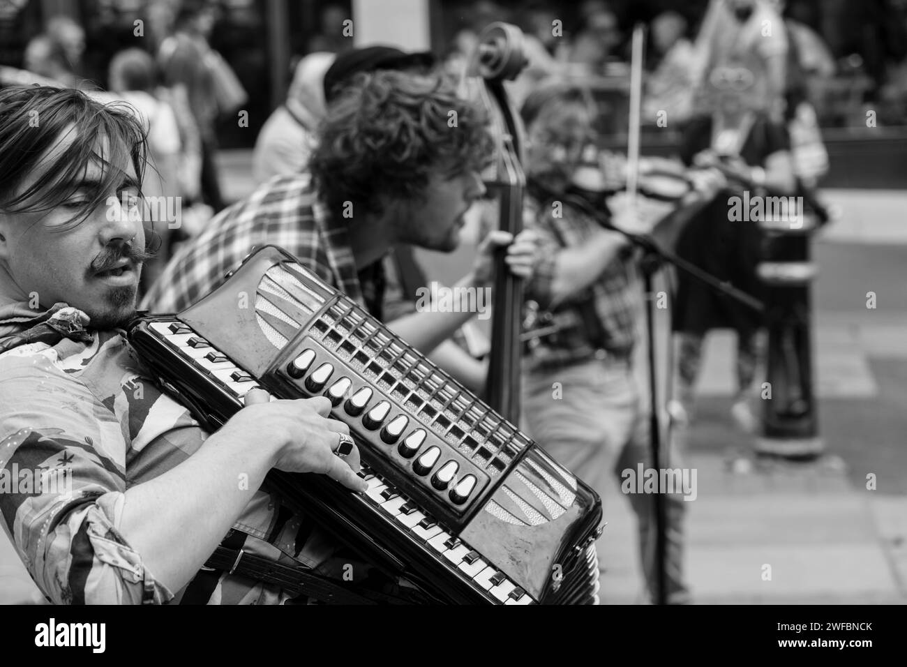 A candid shot of the accordian player with Hyde Family Jam Band busking on a street with the rest of the band, York, UK. Stock Photo