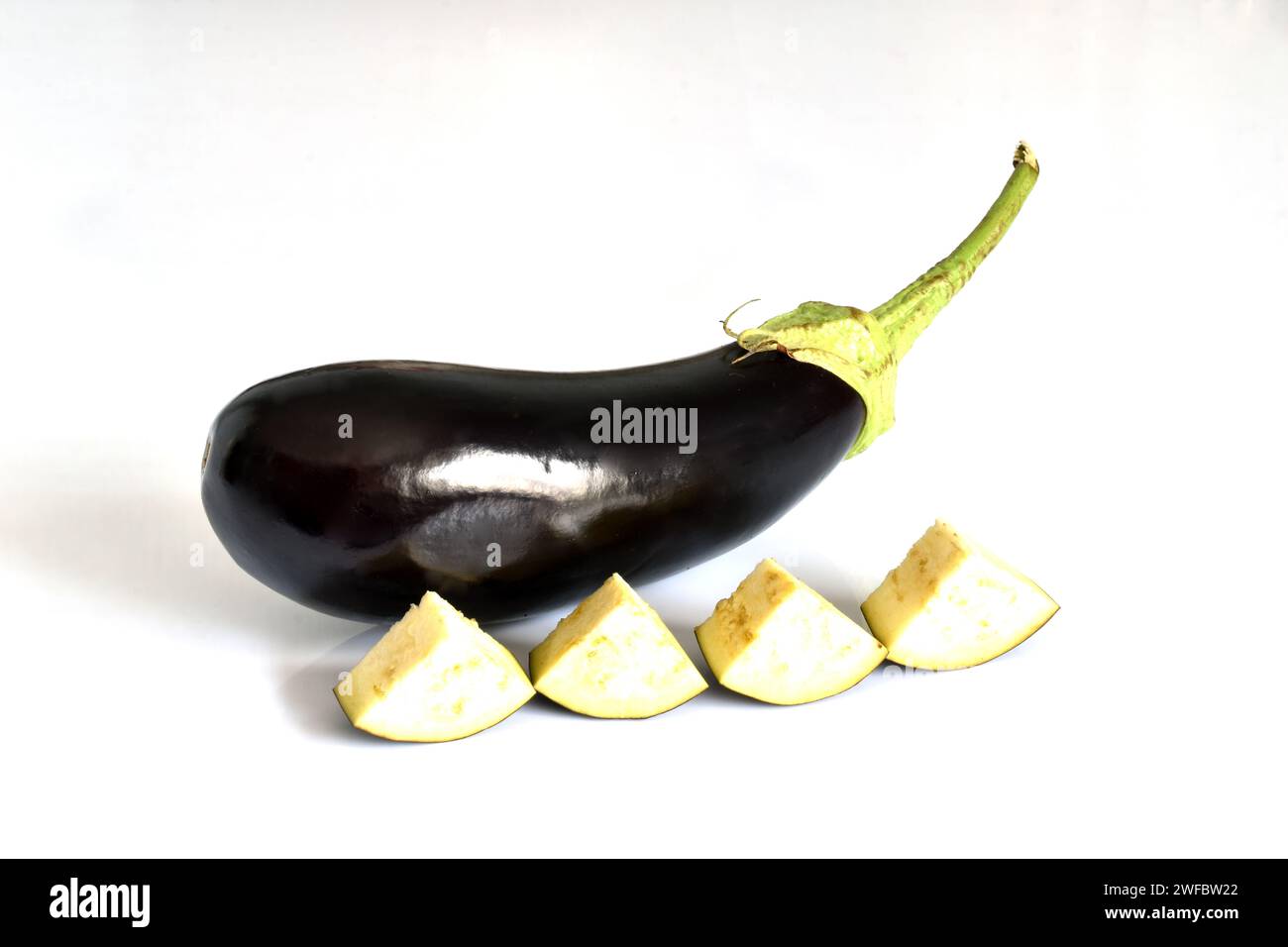 On a white background there is an eggplant vegetable and several pieces cut from another eggplant. Stock Photo