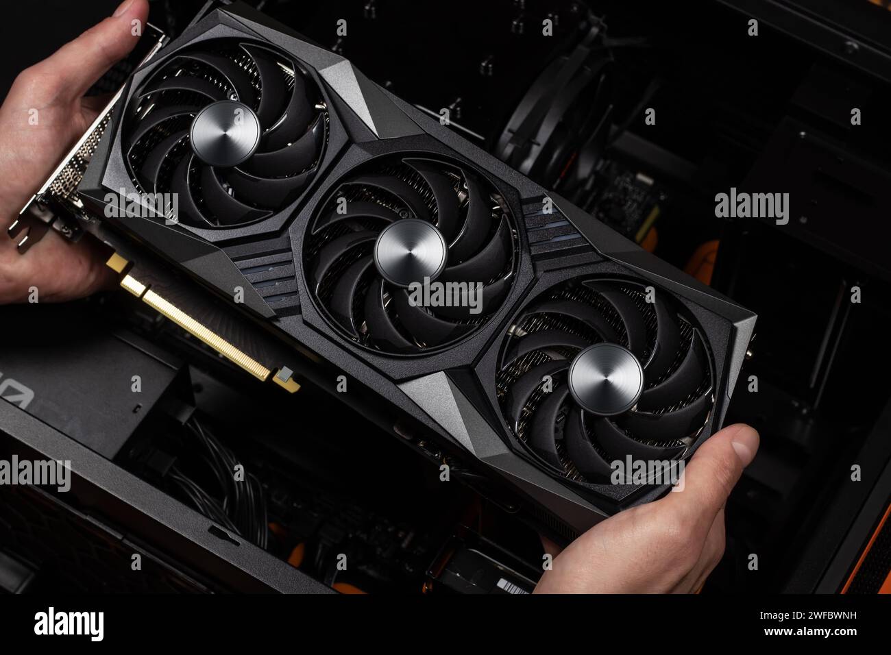Installing video card in an open case of personal computer. Graphics adapter or graphics card in the hand of a technician. PC assembly and upgrade. Stock Photo