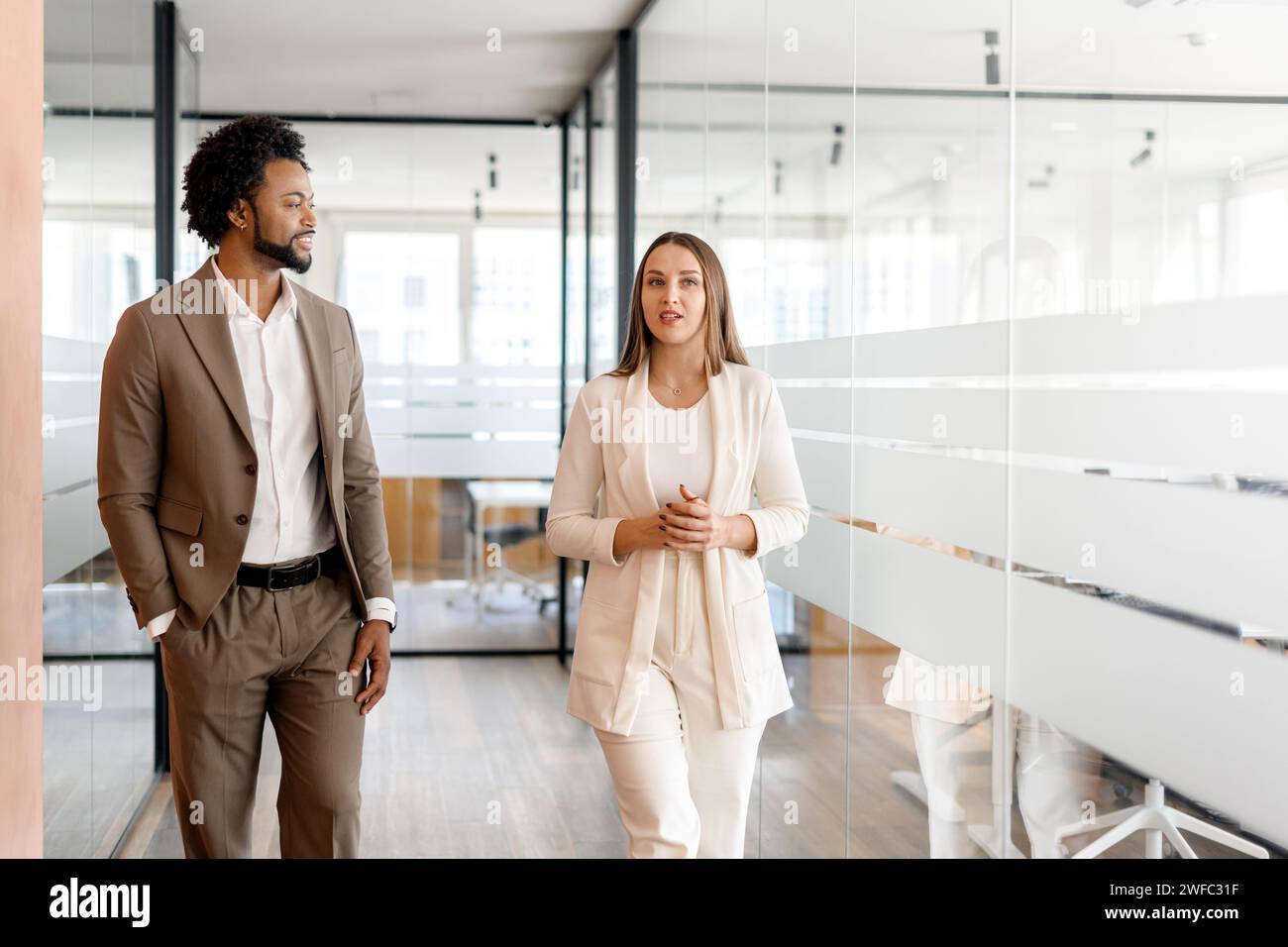 A businesswoman leads the way in an office hallway, with a male colleague alongside her, both exemplifying leadership and a forward-thinking business approach. Teamwork concept Stock Photo