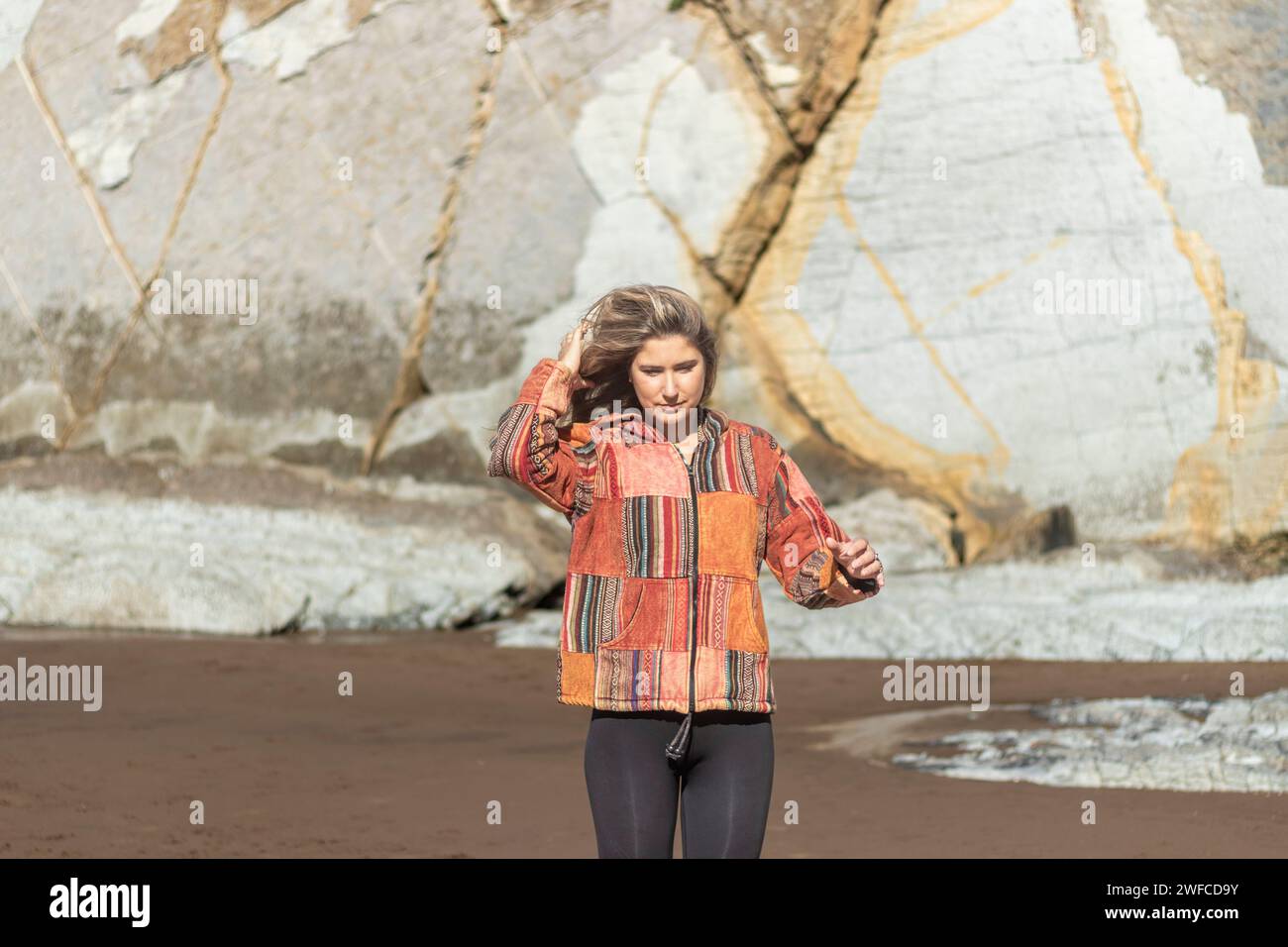 woman in colorful attire stands before a large, patterned rock formation Stock Photo