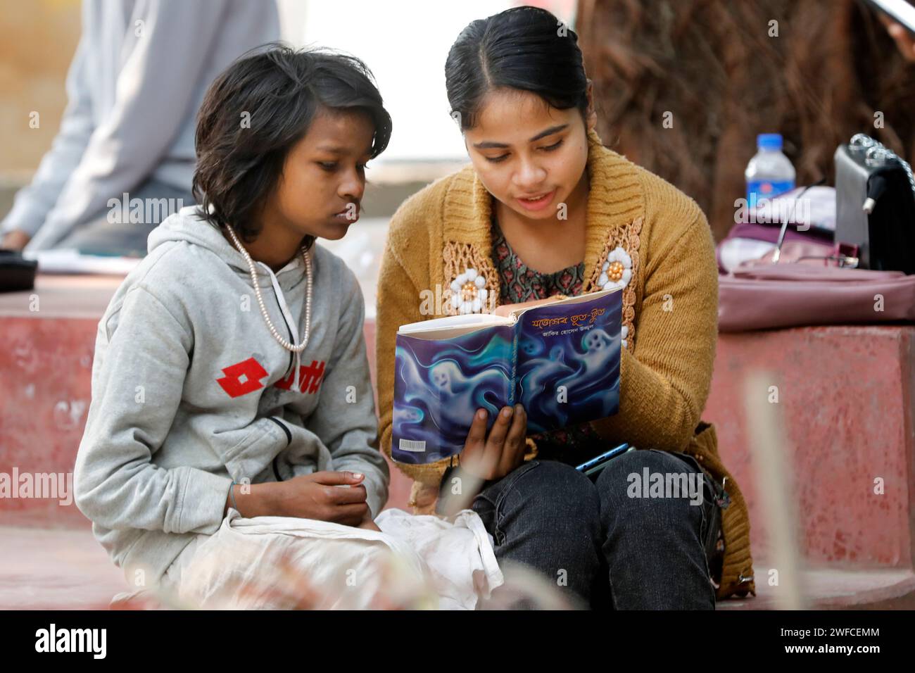 Dhaka, Bangladesh - January 30, 2024: In the open library in front of Dhaka University TSC, a student is reading a story book, while Sumaiya, a street Stock Photo