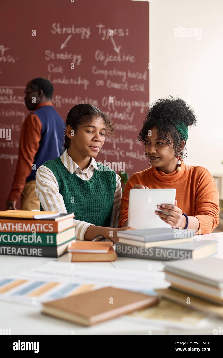 Vertical portrait of two young Black girls using digital tablet together while studying in school classroom Stock Photo