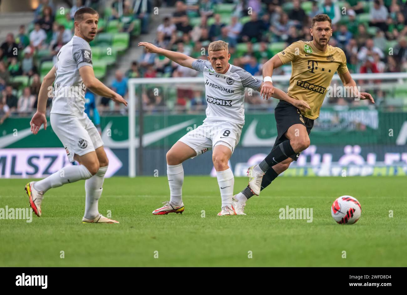 Budapest, Hungary – May 7, 2022. MTK Budapest players Marko Futacs and Mezei Szabolcs with Ferencvaros midfielder Balint Vecsei during Hungarian OTP B Stock Photo
