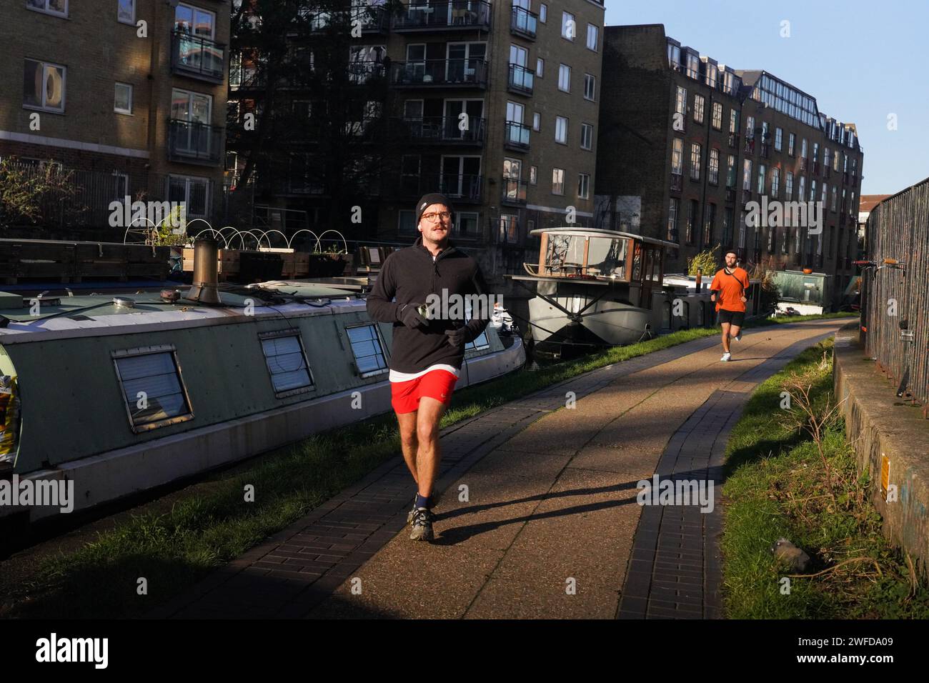 Two men are exercising running along the Regent's Canal in the early morning winter sun. House boats are moored all along the canal. Stock Photo