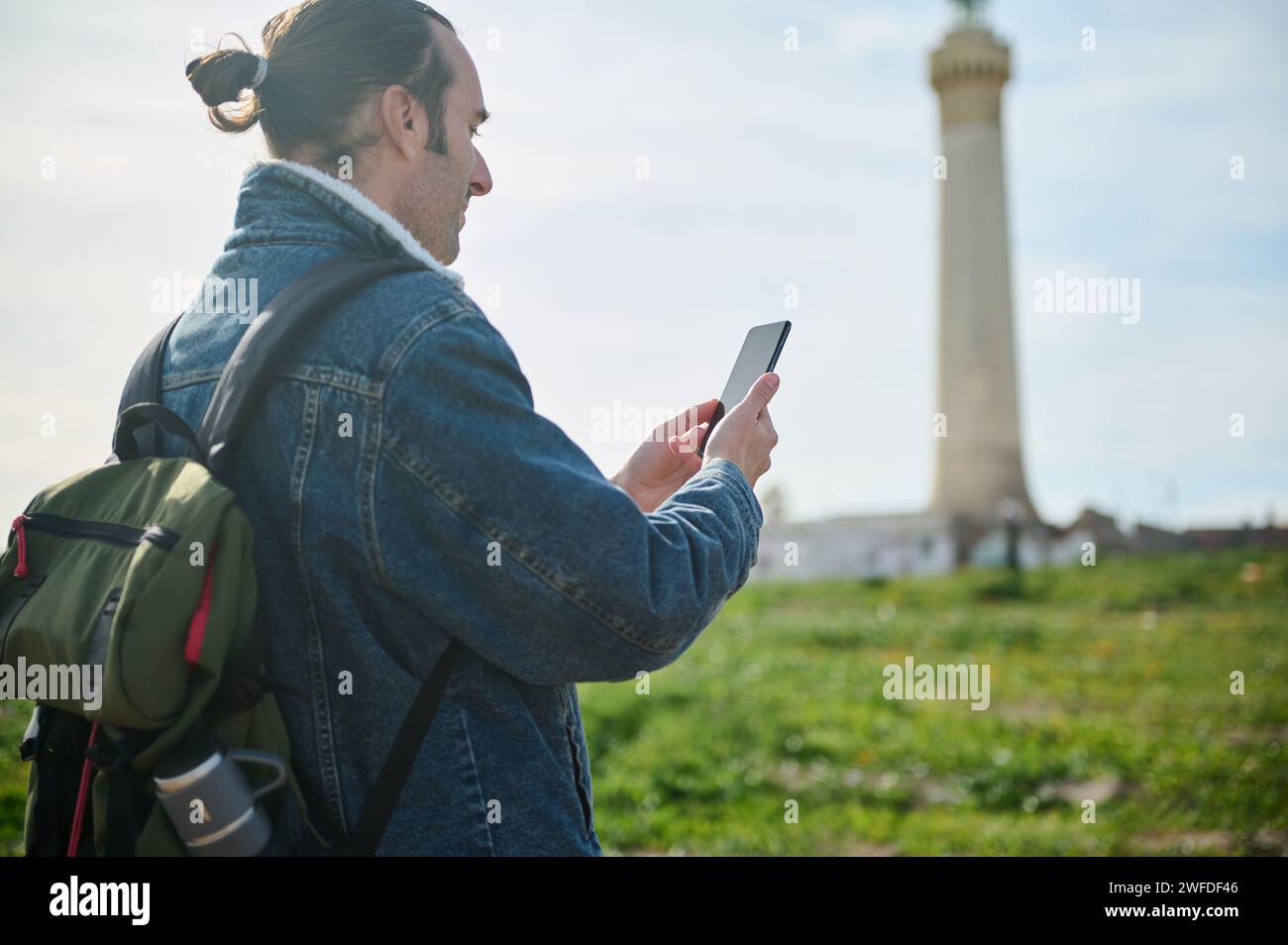 Young adult man traveler tourist hiker adventurer checking mobile application on his smartphone, exploring the nature, standing against the background Stock Photo