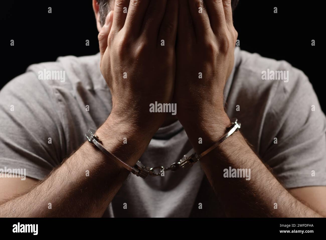 Man, criminal and handcuffs for interrogation, crime or money laundering in arrest on table in room. Closeup of male person, gangster or suspect in ja Stock Photo