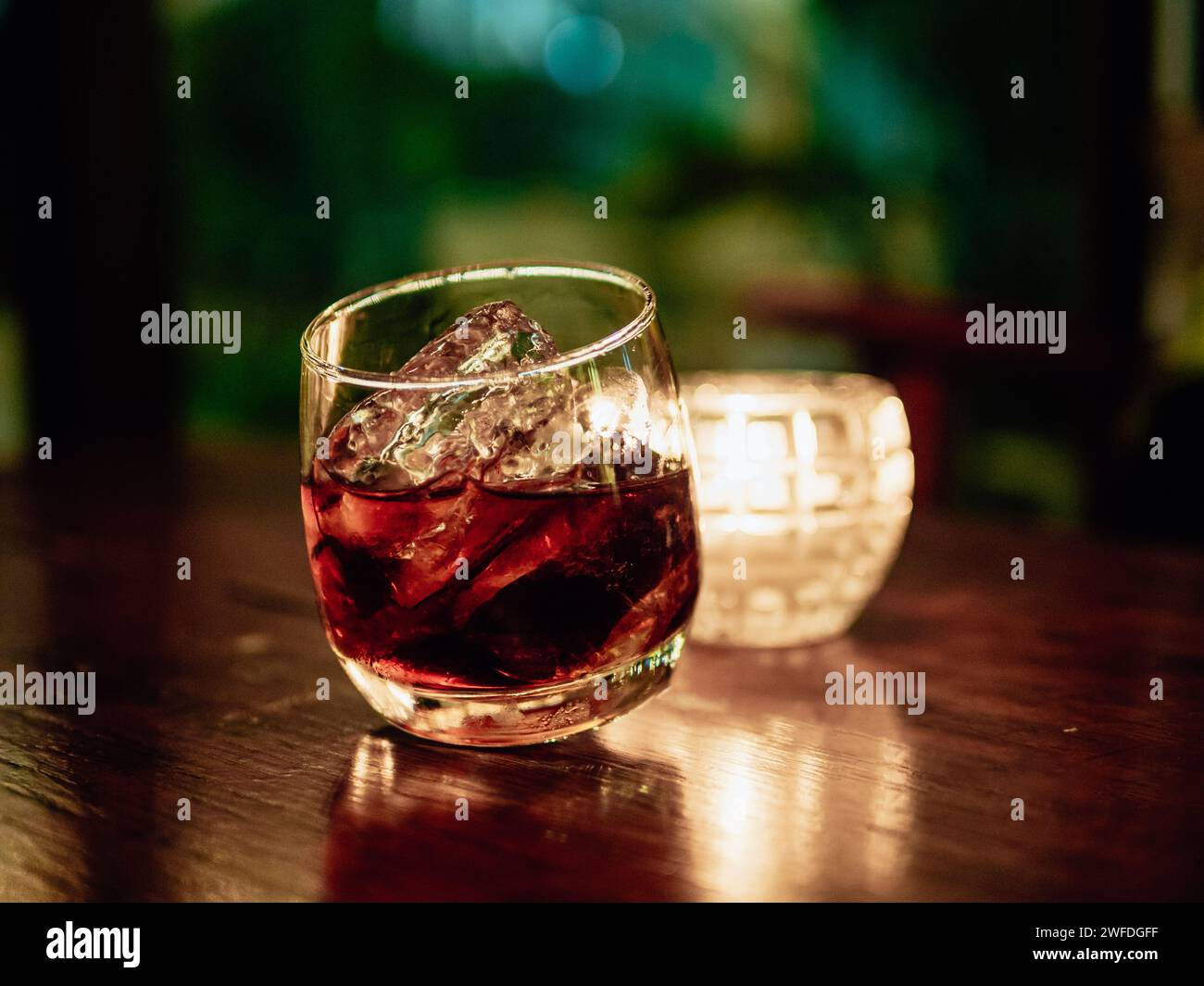 Glass of whisky with ice on wooden table against dark background. Elegant and refreshing glass of scotch bourbon whisky on ice with glowing illuminate Stock Photo