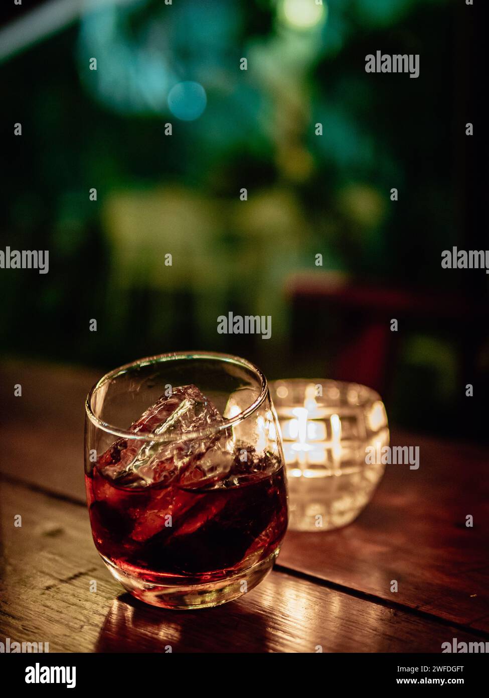 Glass of whisky with ice on wooden table against dark background. Elegant and refreshing glass of scotch bourbon whisky on ice with glowing illuminate Stock Photo