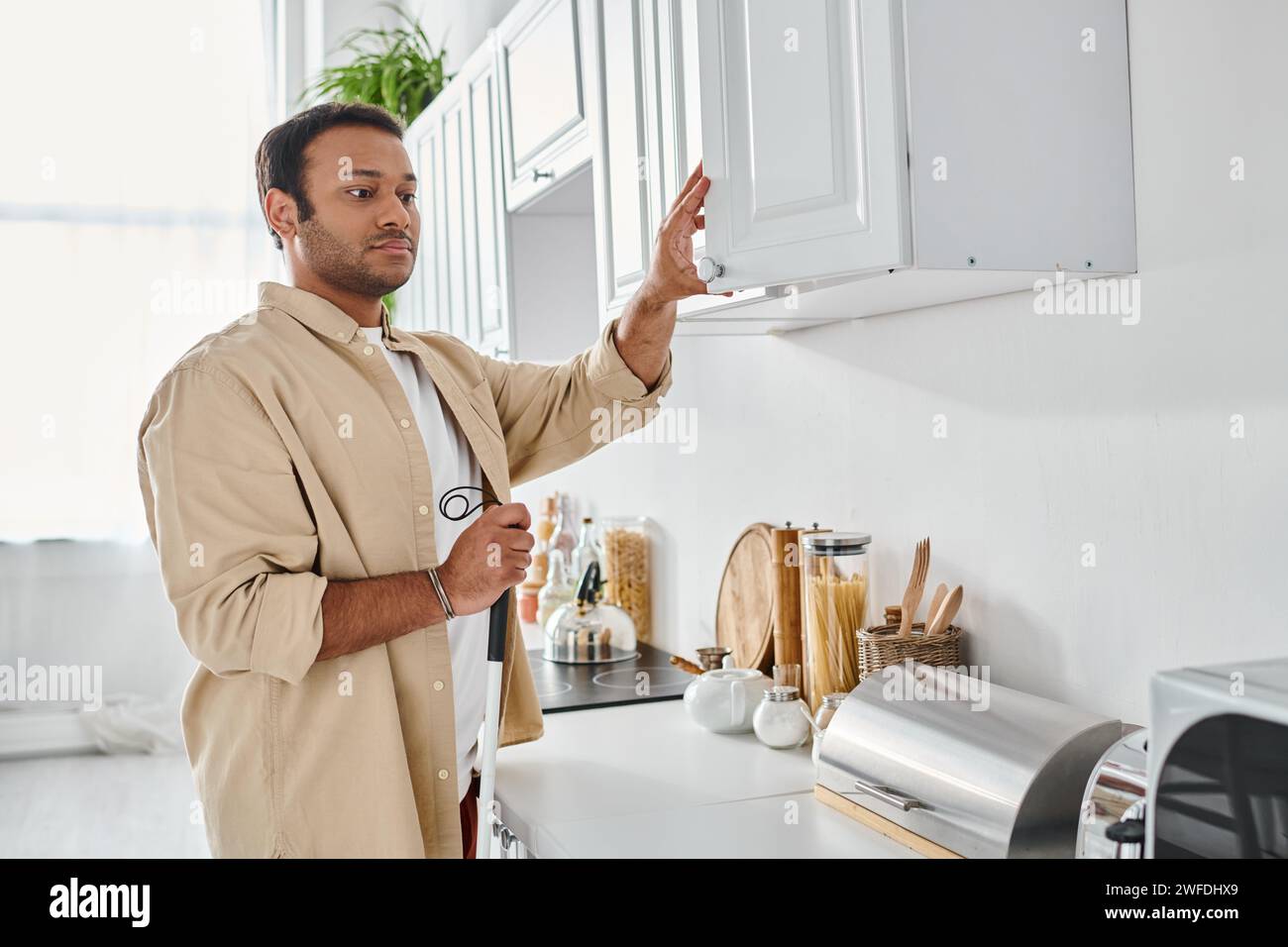 attractive disabled indian man in homewear holding walking stick while preparing food, blind Stock Photo