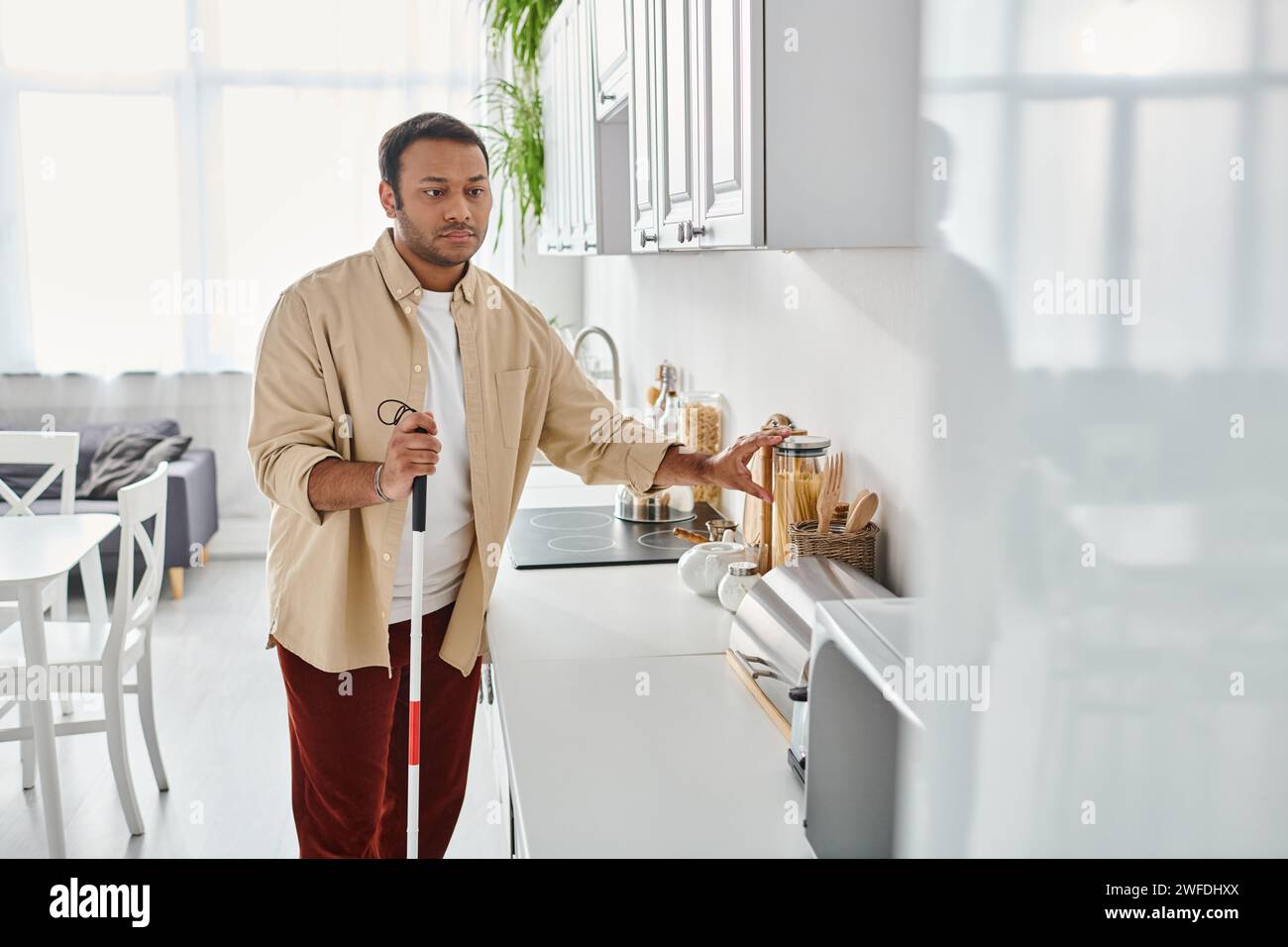good looking disabled indian man in homewear holding walking stick while preparing food, blind Stock Photo