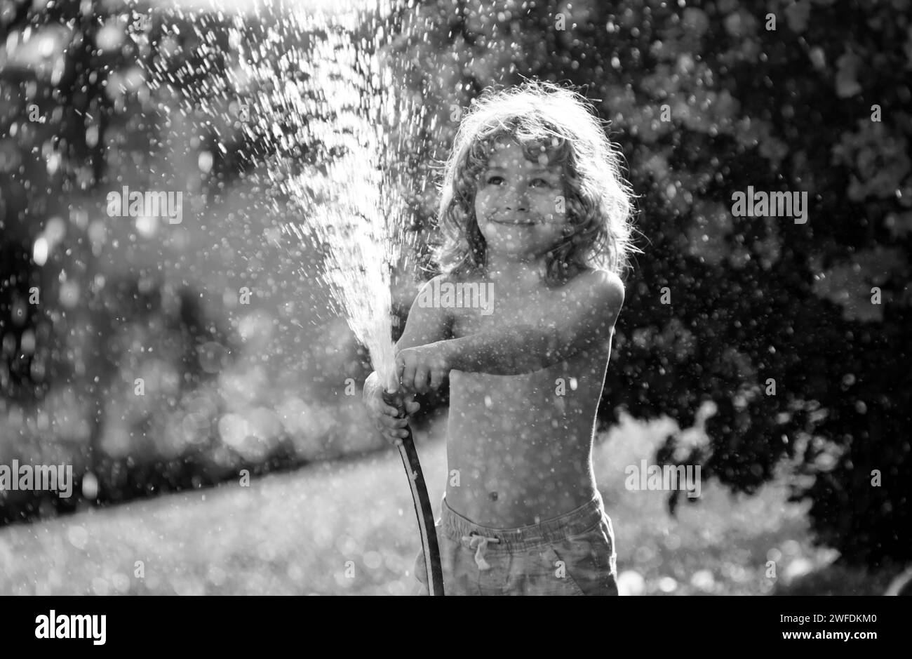 Kid having fun in domestic garden. Child hold watering garden hose. Active outdoors games for kids in the backyard during harvest time. Stock Photo