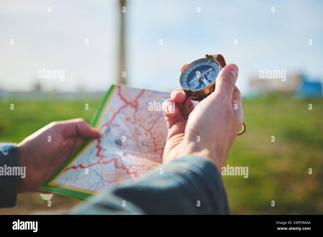 Close-up male hand holds a compass with magnetic arrow showing north direction, over a map while hikes, travels, discovers a new travel destination. P Stock Photo