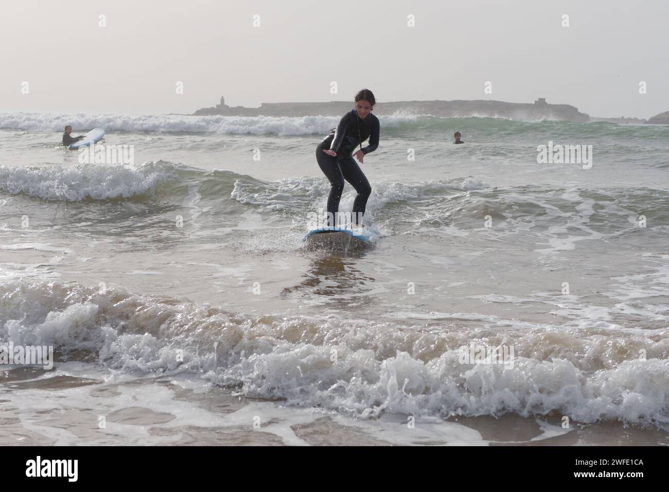 Female surfer rides a wave at sunset with an Island behind in Essaouira ...