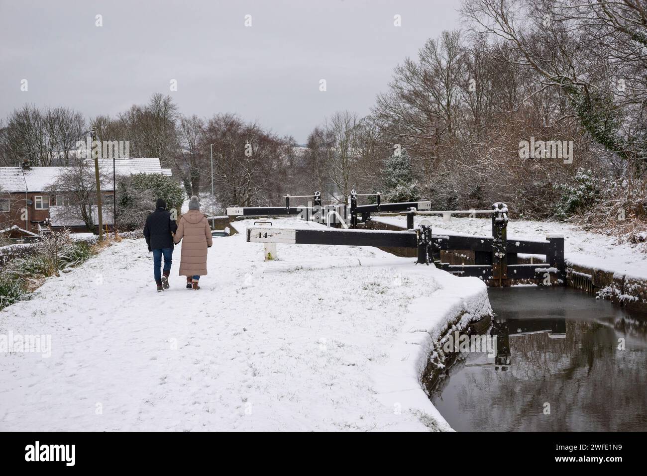 Couple walking next to the Peak Forest Canal at Marple on a snowy January morning. Greater Manchester, England. Stock Photo
