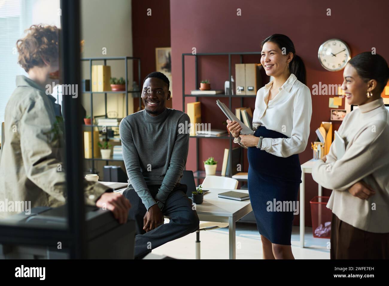 Group of young happy intercultural office managers in quiet luxury attire standing in coworking space and discussing working points Stock Photo
