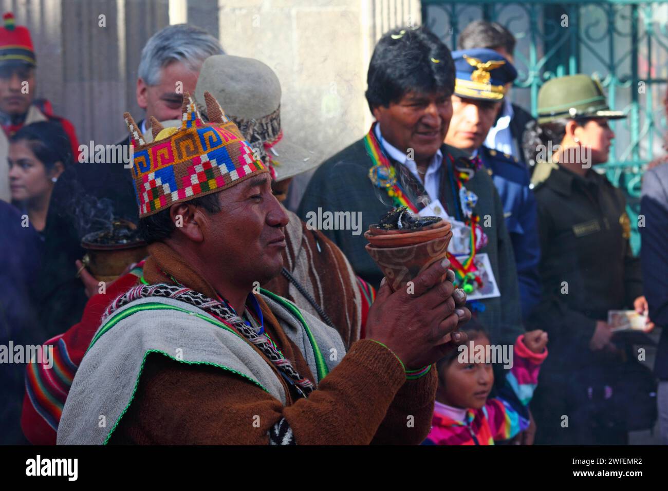 La Paz, BOLIVIA; 24th January 2015. An Aymara amauta or shaman wearing a woollen four-cornered hat performs rituals with an incense burner in front of Bolivian president Evo Morales at an event to mark the start of the Alasitas festival in La Paz. Behind the shaman is the vice president Alvaro Garcia Linera. Stock Photo