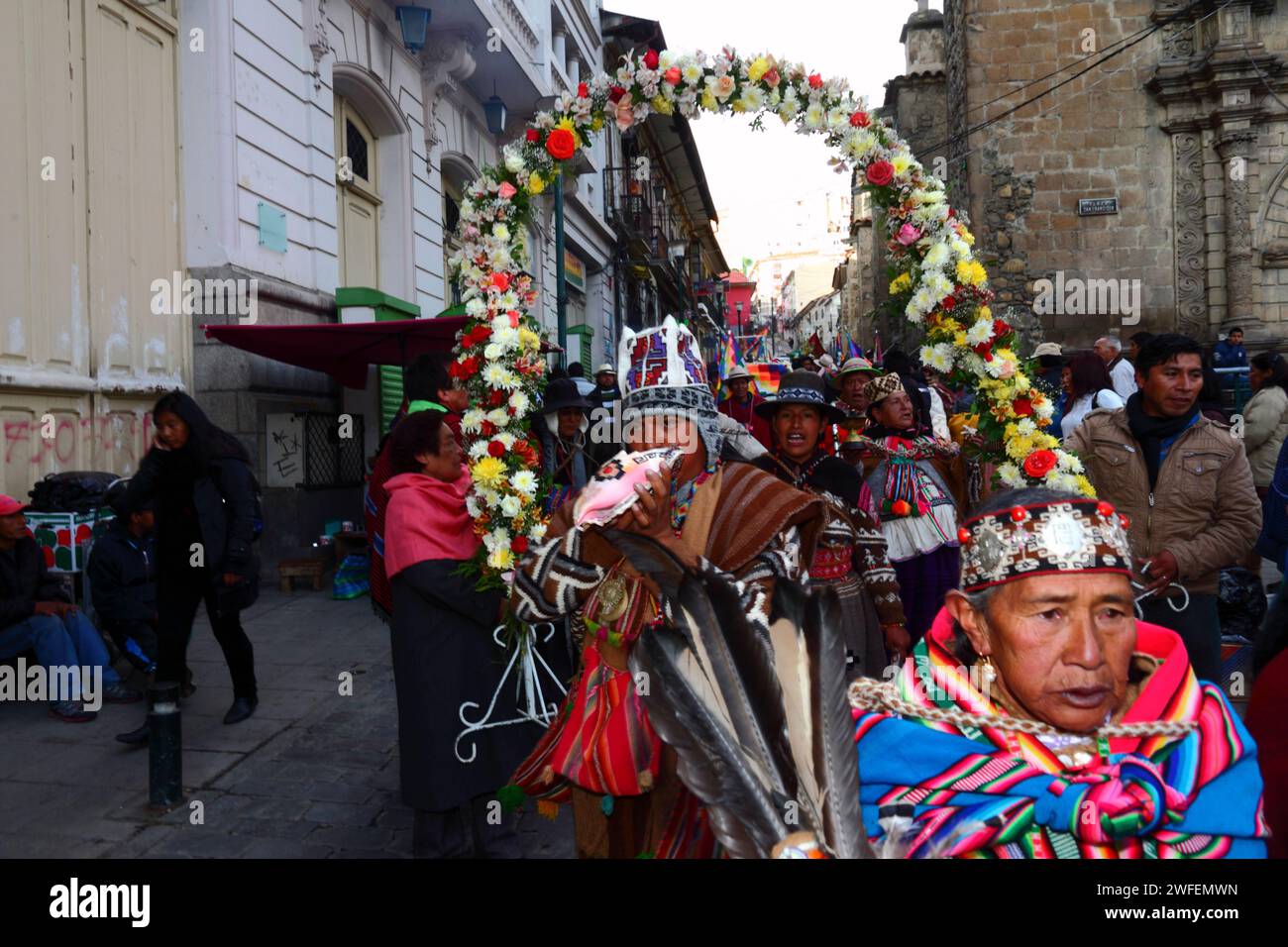 La Paz, BOLIVIA; 24th January 2015. An Aymara shaman blows a conch shell as he walks in front of an ancient illa (or statue) of an Ekeko (an Aymara god of abundance) as it is paraded through the streets of La Paz to celebrate its first appearance at the Alasitas festival, which starts today. The statue is around 2000 years old and was made by the Pucara culture. It was taken from the archaeological site of Tiwanaku to Switzerland in 1858, and returned to Bolivia by the Berne History Museum in November 2014. Stock Photo