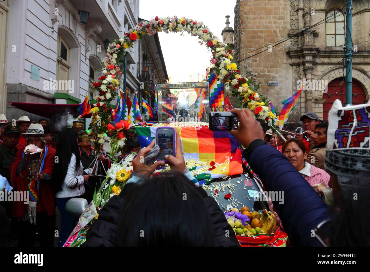 La Paz, BOLIVIA; 24th January 2015. People take photos with their smartphones of an ancient illa (or statue) of an Ekeko (an Aymara god of abundance) as it is paraded through the streets of La Paz to celebrate its first appearance at the Alasitas festival, which starts today. The statue is around 2000 years old and was made by the Pucara culture. It was taken from the archaeological site of Tiwanaku to Switzerland in 1858, and returned to Bolivia by the Berne History Museum in November 2014. On the right is part of San Francisco church. Stock Photo