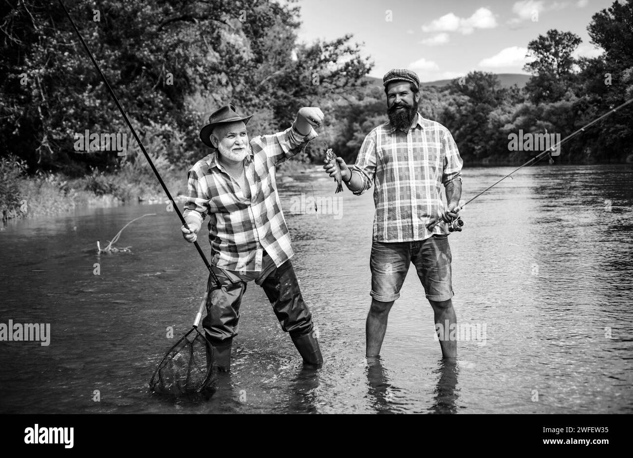 Man friends. Two men friends fishing. Flyfishing angler makes cast, standing in river water. Old and young fisherman. Stock Photo