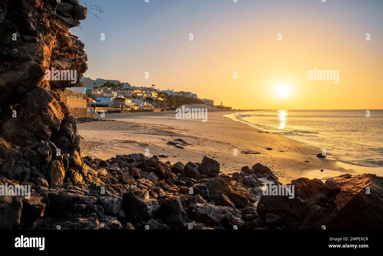 View of a beautiful sunrise light over the volcanic beach Morro Jable framed by the dark lava rocks in the summertime in Fuerteventura, Canary Islands Stock Photo