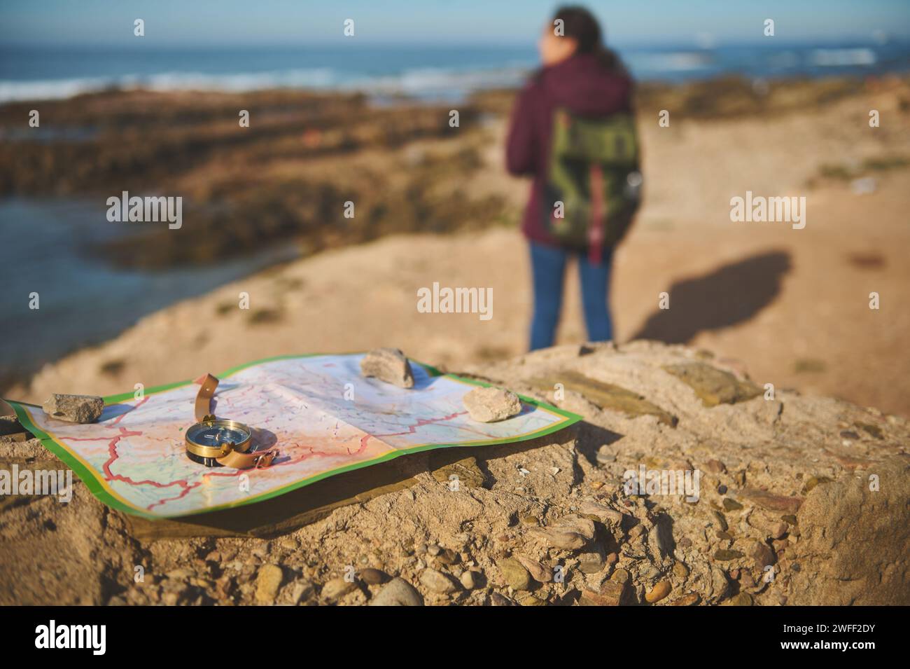 Selective focus on an old vintage golden compass and geographic map on the rock over blurred background of a backpack female tourist enjoying his jour Stock Photo