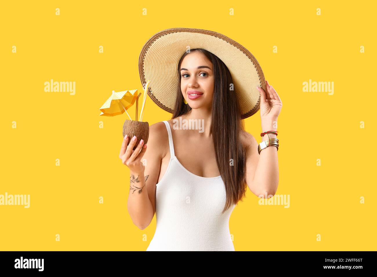 Beautiful young woman with tasty cocktail in coconut on yellow background Stock Photo